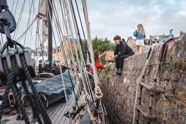 France, Bretagne, 2025-07. In Douarnenez, several volunteers load a ton of cargo consisting of wine, cider, and stills aboard the Grayhound, a replica of a 1776 customs ship. Photographs by Jonathan Cathala / Collectif DR. France, Bretagne, 2025-08. A Douarnenez, plusieurs bénévoles chargent une tonne de cargaison de vin, cidre et alambic à bord du Grayhound, réplique d'un navire douanier de 1776.  Photographies de Jonathan Cathala / Collectif DR.
