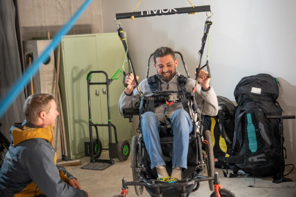 France - Targasonne - 2024-09-05 - Stage de parapente en fauteuil roulant. Alexandre Chevallier règle son fauteuil qui lui servira de sellette en vol. Le parapente est accroché directement au fauteuil via les deux mousquetons latéraux. Les poignées (freins) servent à piloter le parapente en vol. Photographies de Jonathan Cathala / Collectif DR -- France - Targasonne - 2024-09-05 - Paragliding course for wheelchair users. Alexandre Chevallier adjusts his wheelchair, which he uses as a harness in flight. The paraglider is attached directly to the chair using the two side carabiners. The handles (brakes) are used to steer the paraglider in flight. Photographs by Jonathan Cathala / Collectif DR